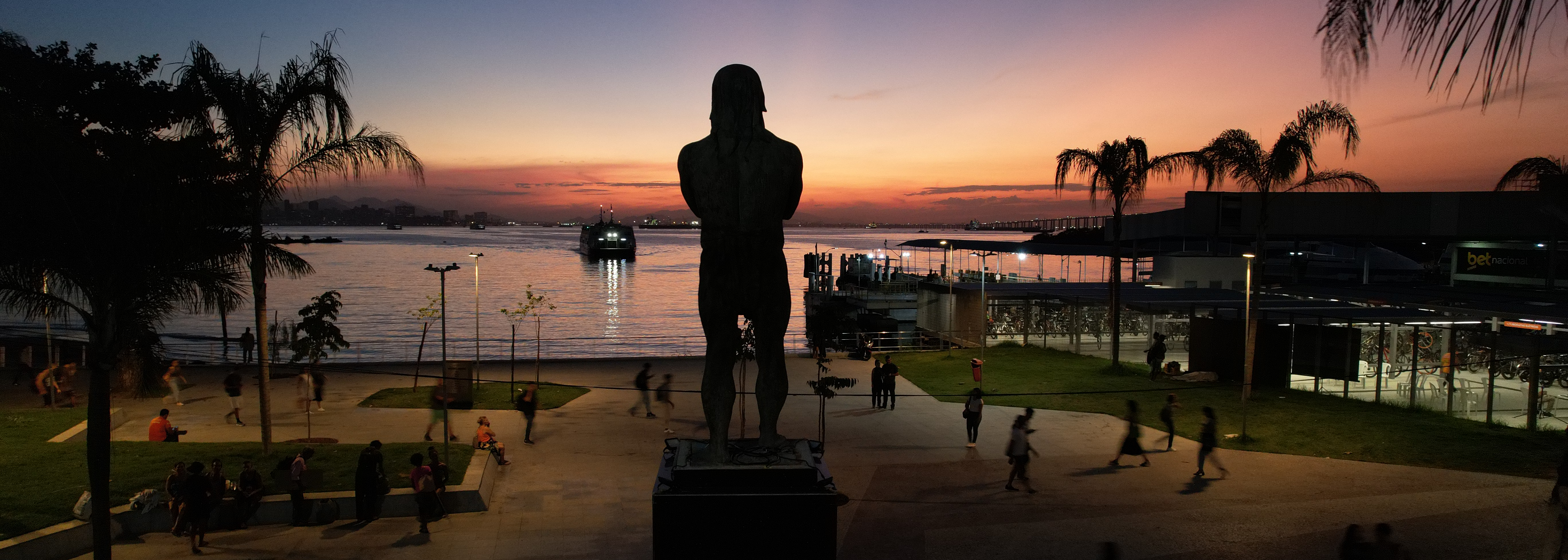 Vista de trás da estátua de Araribóia na Praça Ararabóia, com vista para a Baía de Guanabara ao entardecer.